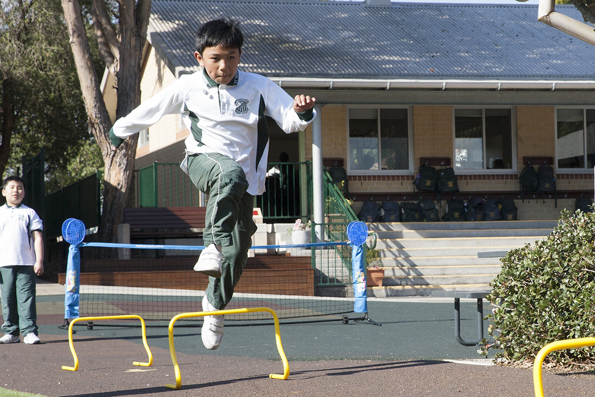 Boy jumping over hurdles in school playground at St Pter Chanel Catholci primary School Regents Park.